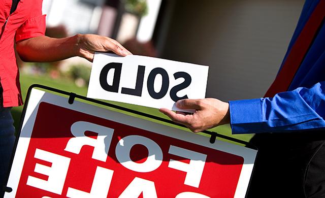 A Texas REALTOR with a client holds a sold sign above a for sale sign in front of a home